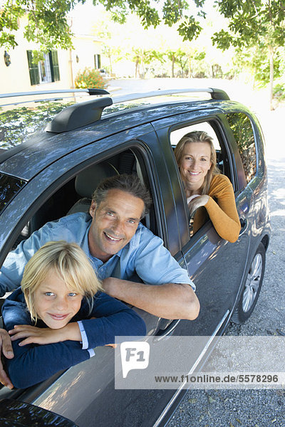 Familie zusammen im Auto  aus den Fenstern lehnend und lächelnd vor der Kamera