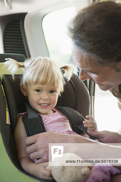 Vater befestigt kleines Mädchen im Autositz