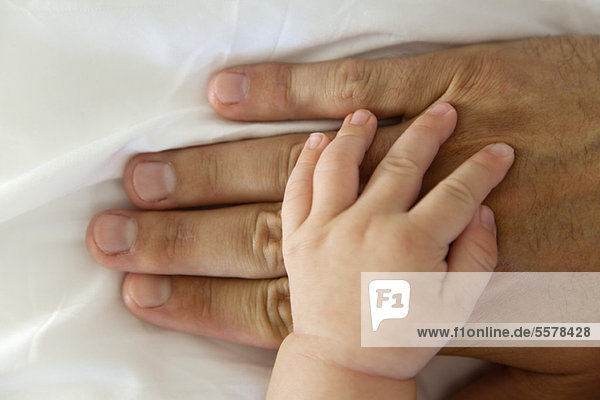 Die Hand des Babys ruht auf der Hand des Mannes.