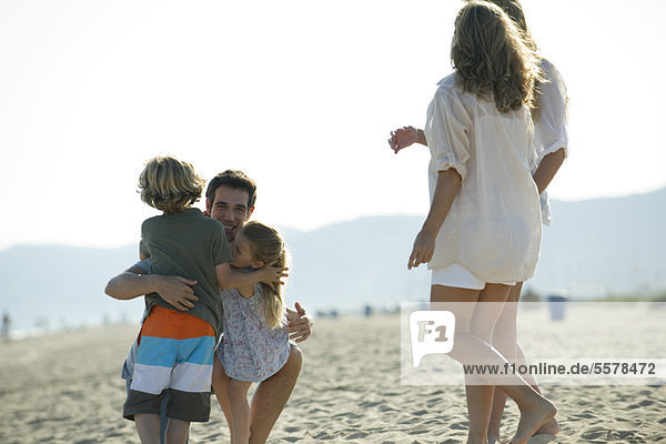 Vater umarmt kleine Kinder am Strand