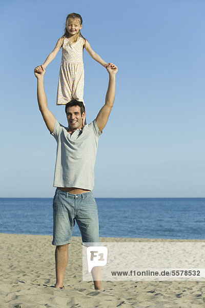 Girl standing on father's shoulders at the beach