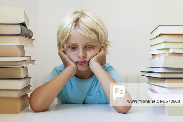 Boy sitting between two stacks of books  sulking