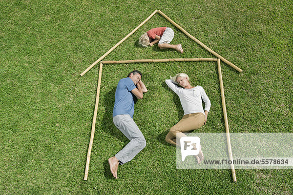 Family with one child lying on grass within outline of house  high angle view