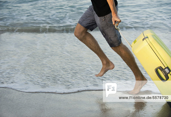 Mann läuft am Strand mit Koffer