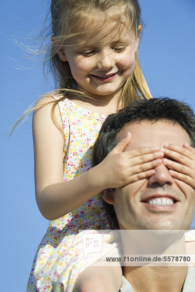 Mädchen  das Vaters Augen mit ihren Händen bedeckt.