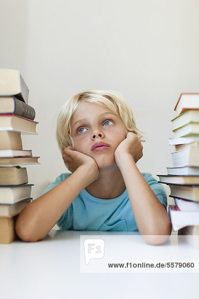 Boy sitting between two stacks of books  daydreaming