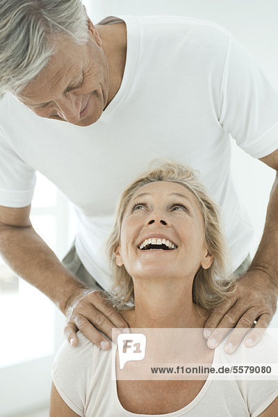 Ein reifes Paar lächelt sich an  während der Mann die Schultern der Frau massiert.