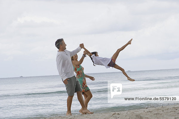 Parents swinging daughter while walking on beach