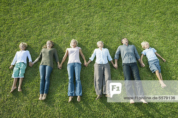 Group lying side by side on grass holding hands