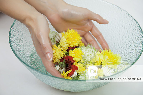 Frau tränkt die Hände in einer Schüssel mit Wasser und Blumen  abgeschnitten