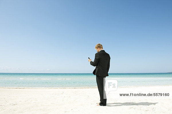 Geschäftsmann mit Handy am Strand