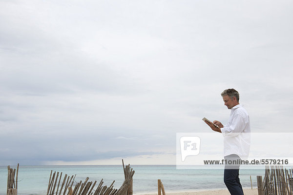 Erwachsener Mann mit digitalem Tablett am Strand