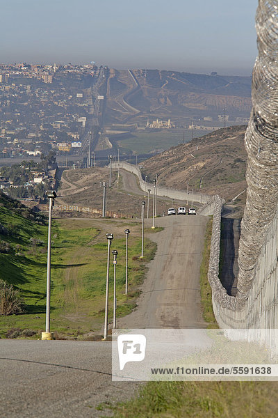 Three U.S. Border Patrol vehicles patrol the international border between the United States and Mexico  with the Border Patrol's new fence at right and Tijuana on the left  San Ysidro  California  USA