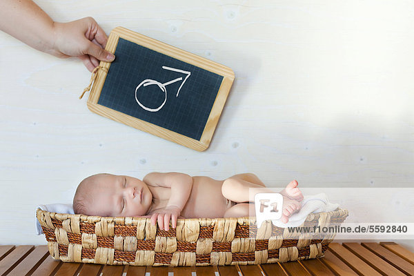 Neugeborenes Baby  3 Wochen  schlafend in Korb  Hand hält Tafel mit Marssymbol darüber