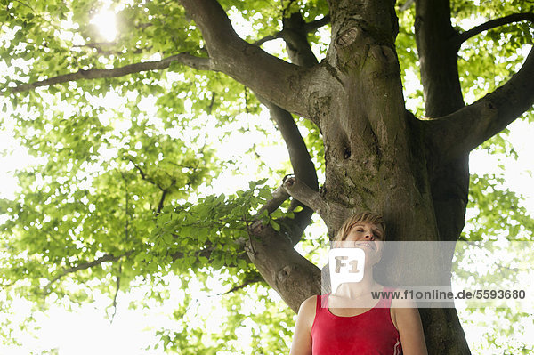 Mittlere erwachsene Frau auf einem Baum ruhend  lächelnd