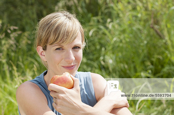 Mittlere erwachsene Frau beim Apfelessen  lächelnd  Porträt