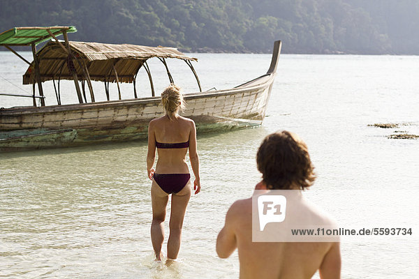 Thailand  Koh Surin  Young couple walking in water towards boat