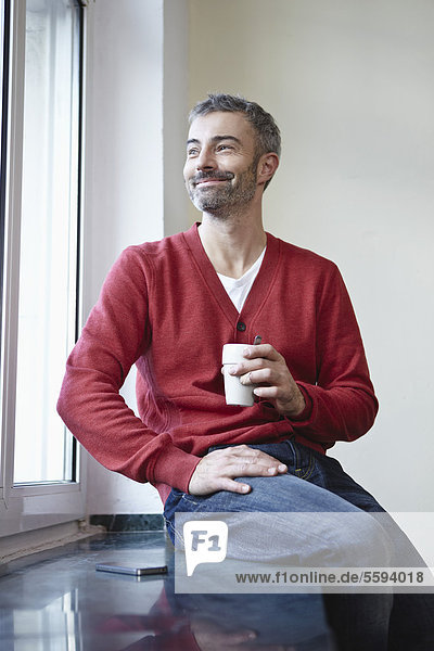 Reifer Mann am Fenster sitzend mit Kaffee  lächelnd