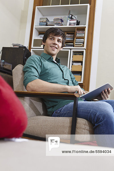 Junger Mann mit digitalem Tablett auf Stuhl  lächelnd