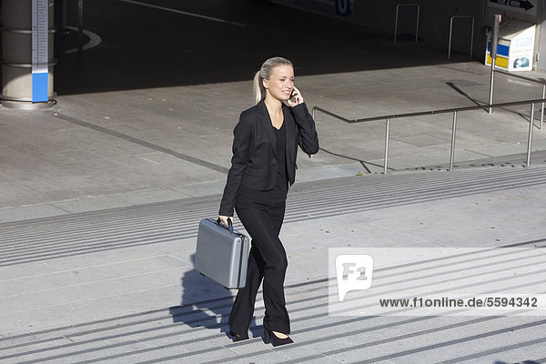 Businesswoman on stairs with briefcase and talking on cell phone  smiling
