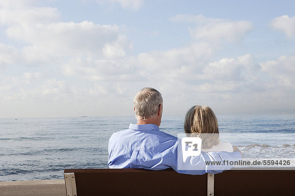 Spanien  Mallorca  Seniorenpaar auf Bank am Meer sitzend