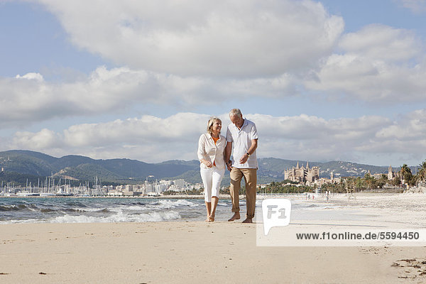 Spanien  Mallorca  Seniorenpaar am Strand entlang  lächelnd