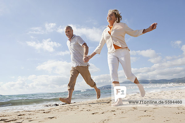 Spanien  Mallorca  Seniorenpaar am Strand entlang  lächelnd
