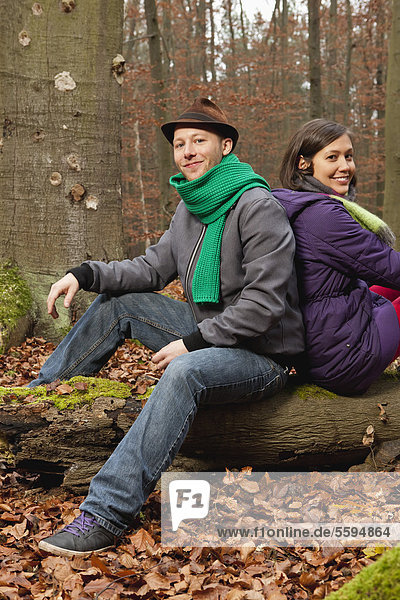 Deutschland  Berlin  Wandlitz  Paar auf Baumstamm sitzend  lächelnd  Portrait