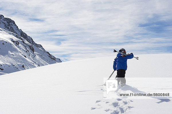 Child carrying skis up snowy mountain