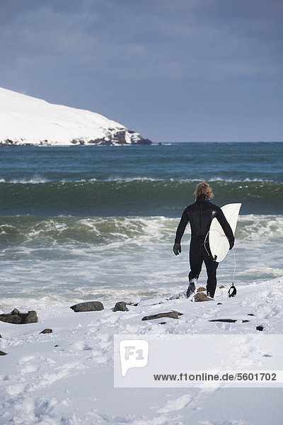 Surfer carrying surfboard on snowy beach