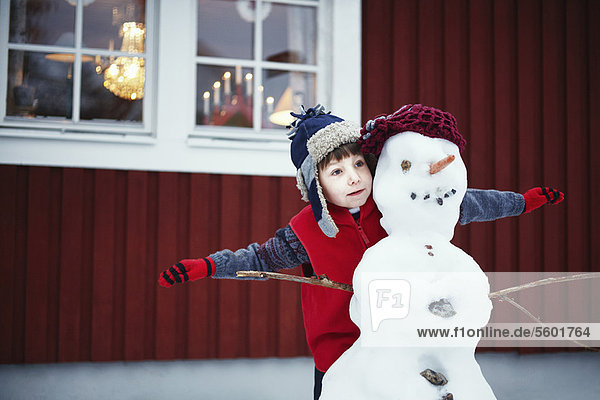 Junge spielt mit Schneemann im Freien