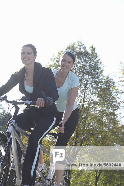 Smiling women riding tandem bicycle