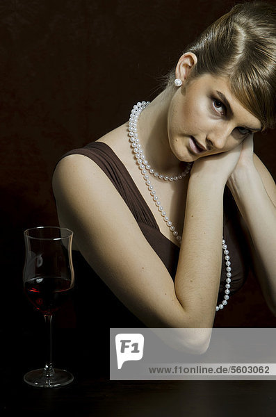Junge Frau mit Perlenkette und Perlenohring  daneben Rotwein im Rotweinglas