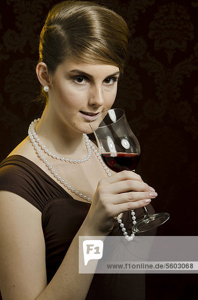 Young woman wearing a pearl necklace and pearl earrings  drinking red wine in a wine glass