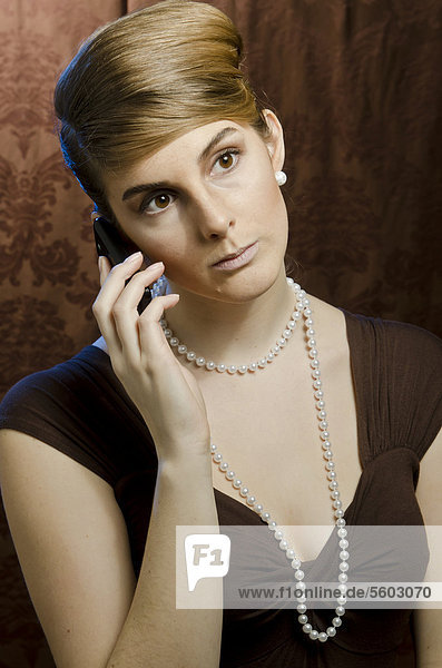 Junge Frau mit Perlenkette und Perlenohring  telefoniert mit Handy