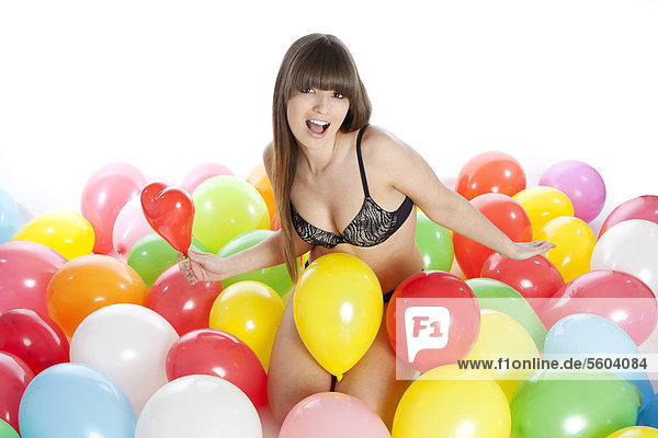 Junge Frau in Dessous sitzt zwischen bunten Luftballons und schreit vor Freude