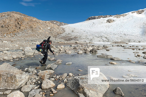 Leader of a group of hikers with a backpack and a rifle at the river-crossing at Mittivakkat Glacier  Peninsula Ammassalik  East Greenland  Greenland