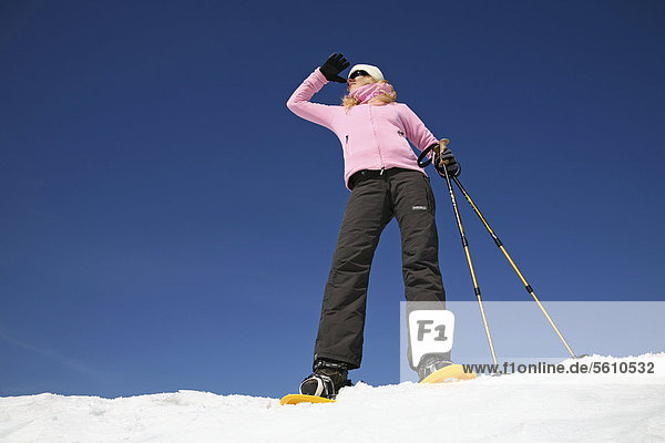 Junge Frau  etwa 25 Jahre  beim Schneeschuhfahren mit Stöcken in der Hand  vor stahlblauem Himmel  Thüringer Wald  Thüringen  Deutschland  Europa
