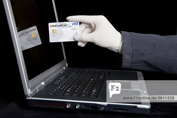 Hacker using a laptop  holding a Visa card and wearing latex gloves to leave no traces  symbolic image for Internet crime