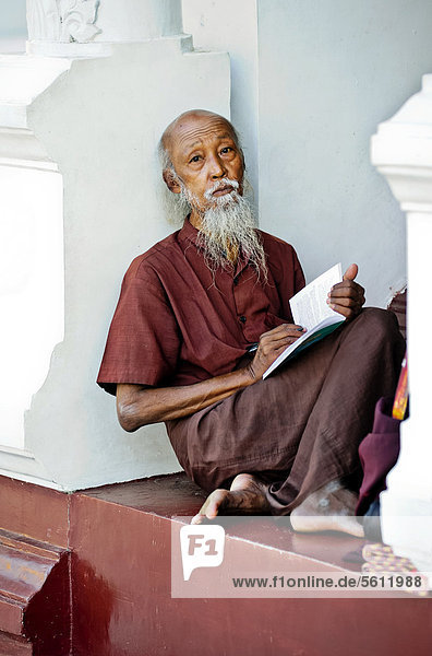 Lesender Mönch sitzt zwischen Säulen bei der Shwedagon Pagode in Yangon  Myanmar  Birma  Südostasien  Asien