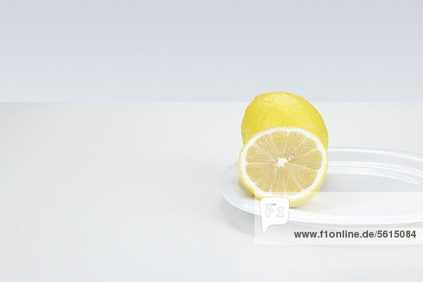 Zitronen (Citrus limon)  ganz und halbiert  auf einem weißen Teller