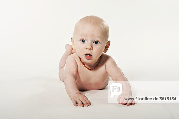 Auf Bauch liegendes Baby  Junge  8 Monate  mit Bernsteinkette  erstaunt schauend