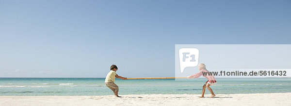 Kinder beim Tauziehen mit Bambus am Strand