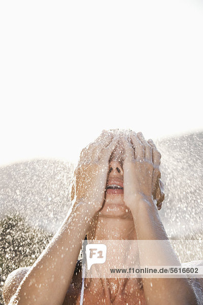 Woman washing face under shower outdoors