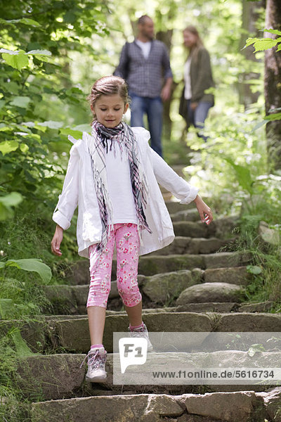 Girl walking down stone steps in woods  parents in background