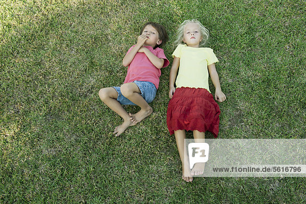 Kinder liegen zusammen auf Gras und schauen in die Kamera.