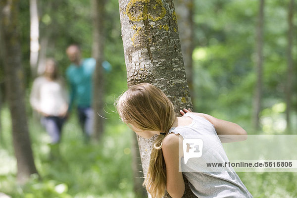 Girl hiking behind tree in woods