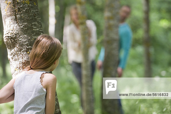 Girl playing hide and seek with parents in woods  rear view