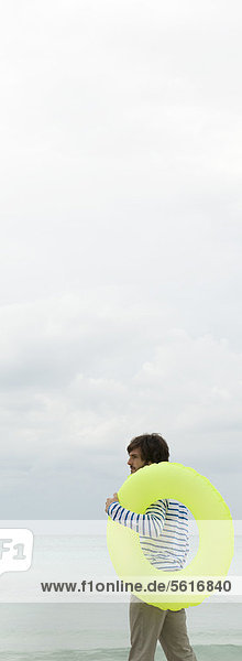 Junger Mann mit aufblasbarem Ring  Blick auf den Ozean