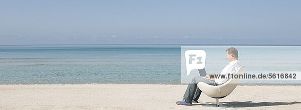 Mann mit Laptop am Strand